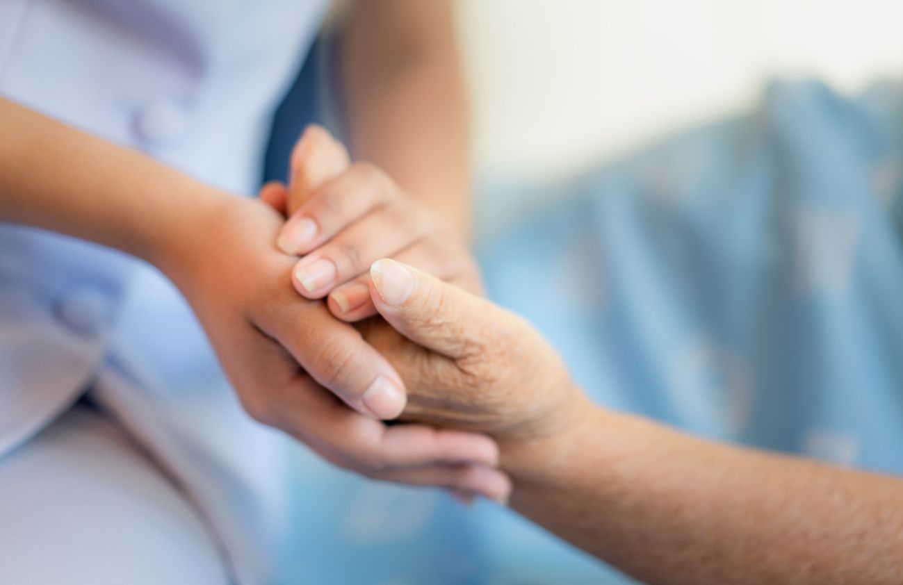 Eine Krankenschwester hält die Hand einer älteren Person und zeigt damit Fürsorge und Unterstützung.